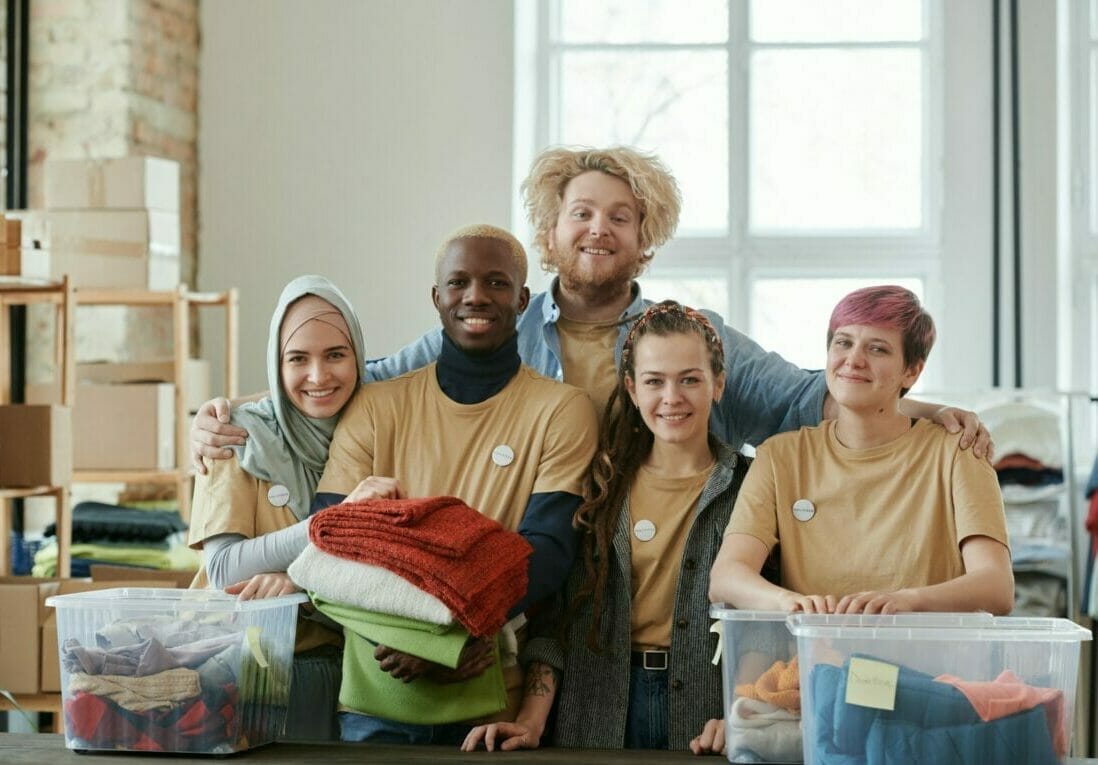 A Group Of Volunteers Sorting Clothes Into Containers Posing Together